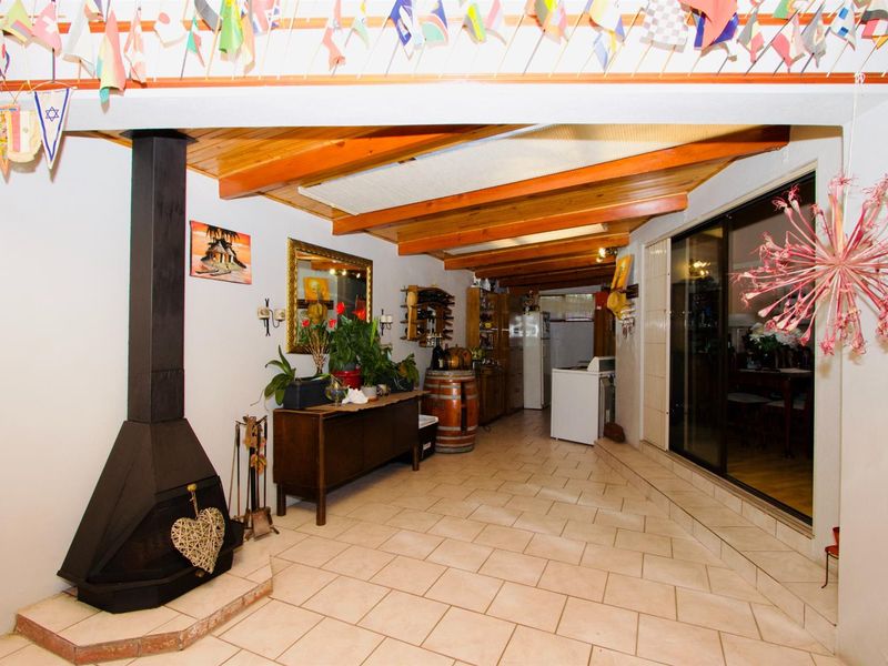 Covered patio area featuring a built-in fireplace, exposed timber ceiling beams, and tiled flooring, providing a versatile space for outdoor living.