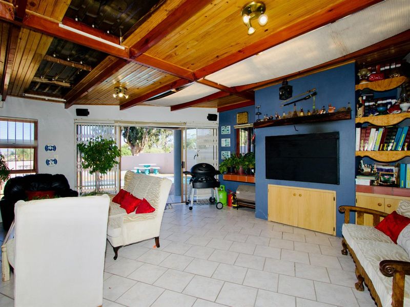 Spacious open-plan living area featuring tiled flooring, exposed timber beam ceiling, and built-in shelving, with direct access to the outdoor patio area.