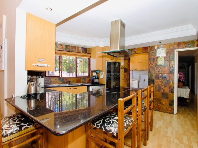 A functional kitchen featuring a large black granite breakfast bar, built-in oven, extractor fan, and natural stone wall tiling.