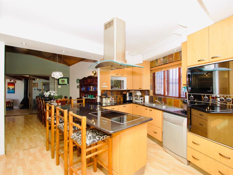 Open-plan kitchen featuring light wood cabinetry, granite countertops, a central island with a built-in hob, and integrated stainless steel oven and extractor fan.