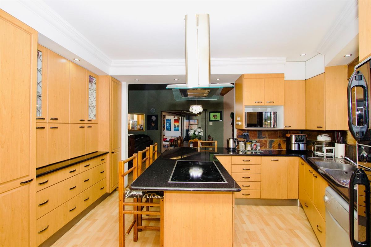 A functional kitchen featuring light wood cabinetry, black granite countertops, a central island with an integrated electric hob, and a stainless steel extractor fan.