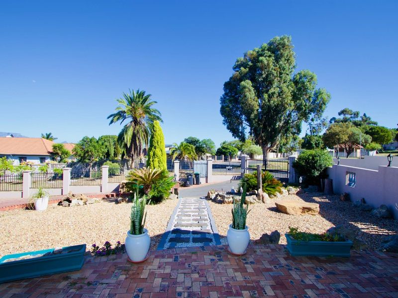 A view from the patio looking out over a landscaped garden with a paved walkway, gravel beds, and perimeter fencing.