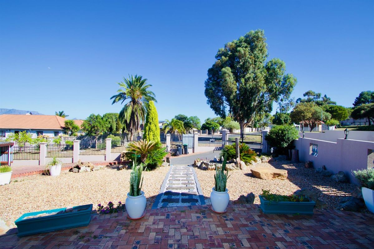 A view from the patio looking out over a landscaped garden with a paved walkway, gravel beds, and perimeter fencing.