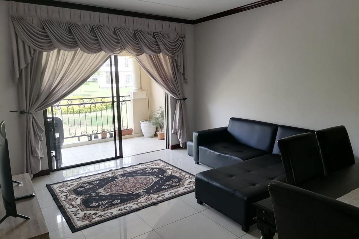 A bright living room featuring large sliding glass doors that open onto a private balcony, finished with neutral floor tiles and crown molding.