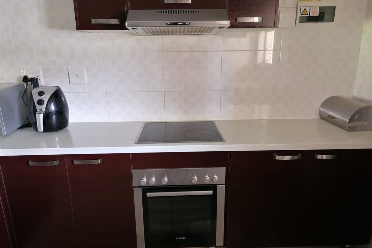 A functional kitchen area featuring dark wood cabinetry, a built-in Bosch oven, electric hob, and stainless steel extractor fan with tiled splashback.