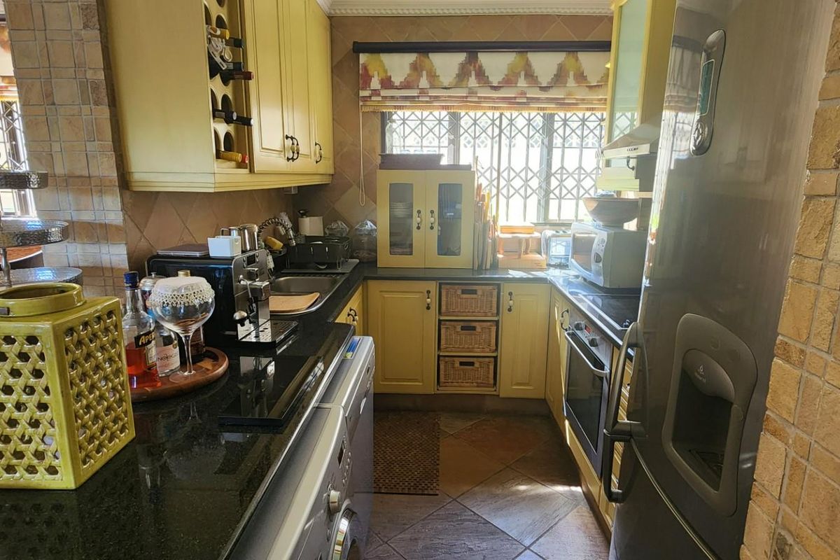 Compact kitchen featuring yellow cabinetry, dark granite countertops, tiled flooring, and integrated oven with security bars on the window.