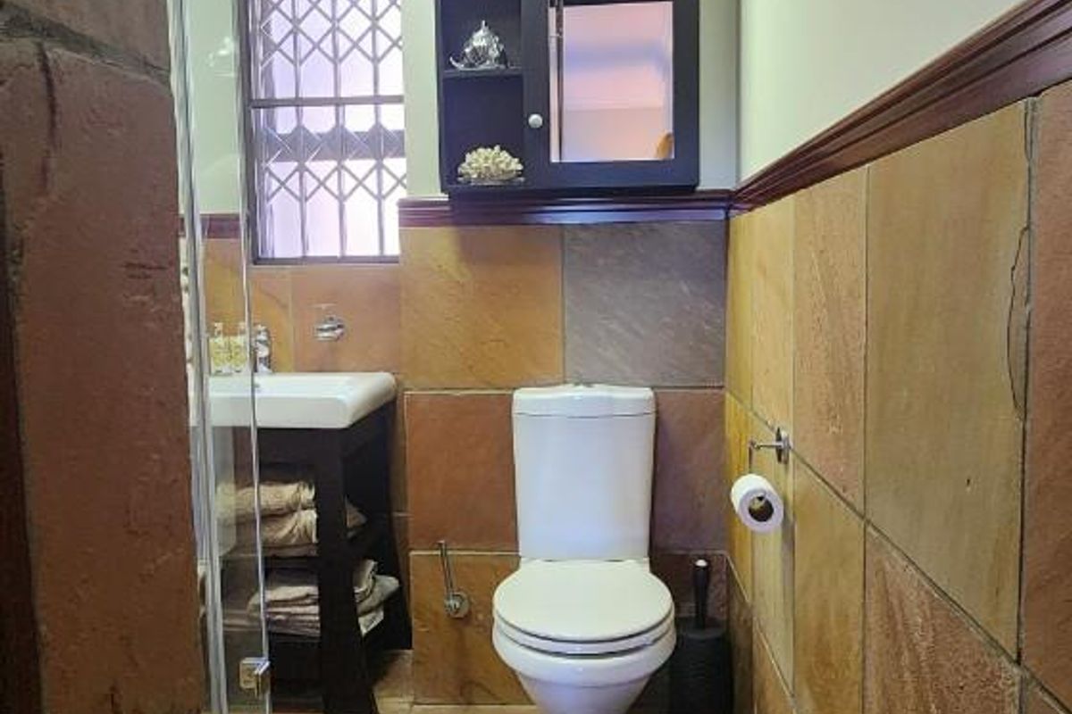 A compact bathroom featuring natural stone wall and floor tiles, a pedestal basin, a toilet, and a glass-enclosed shower area.