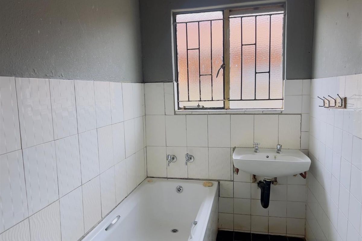 A functional bathroom featuring a bathtub, wall-mounted basin, and security bars on the window, requiring cosmetic updates to improve its overall condition.