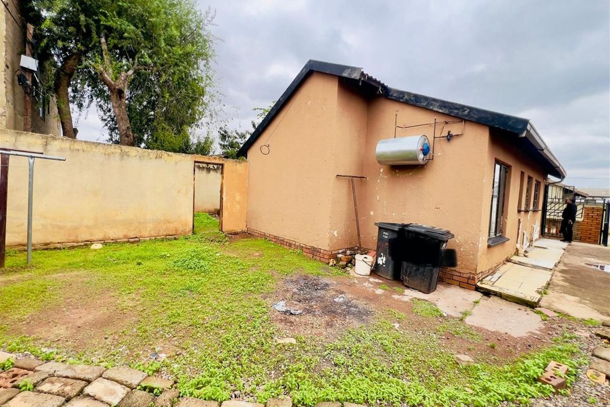 Rear exterior view of the property featuring a small garden area, boundary wall, and external geyser unit.