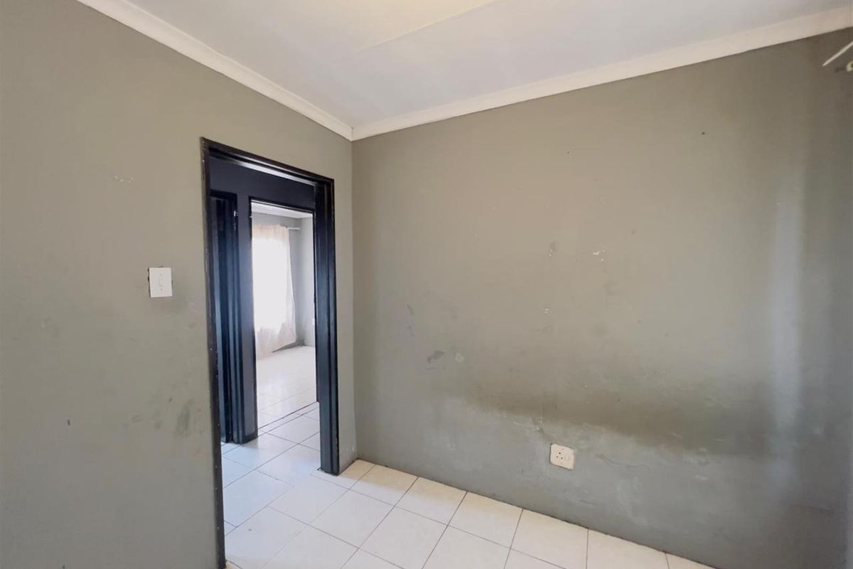 An empty bedroom featuring tiled flooring and neutral grey walls, showing signs of wear and requiring cosmetic updates.