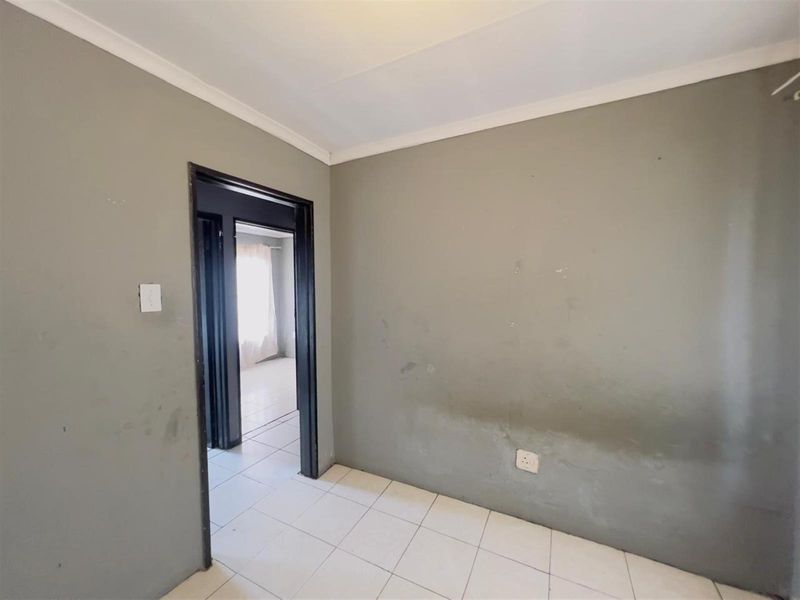 An empty bedroom featuring tiled flooring and neutral grey walls, showing signs of wear and requiring cosmetic updates.