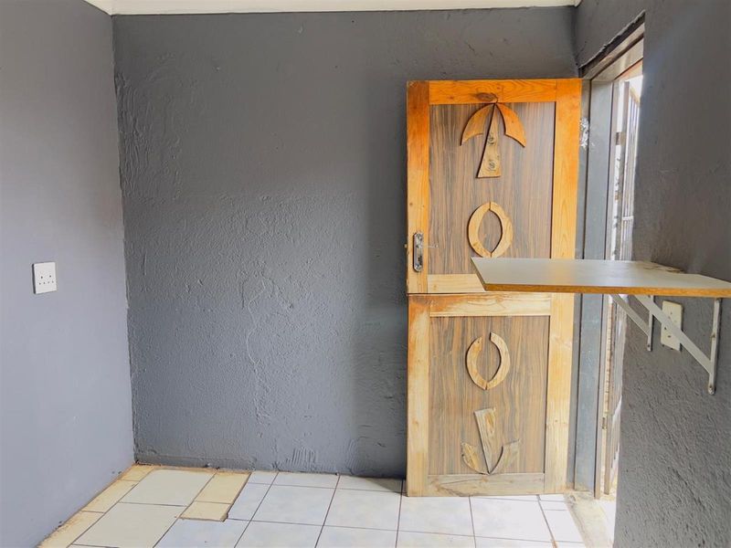 A small utility space featuring a unique stable-style wooden door, ceramic tiled flooring, and a wall-mounted shelf.