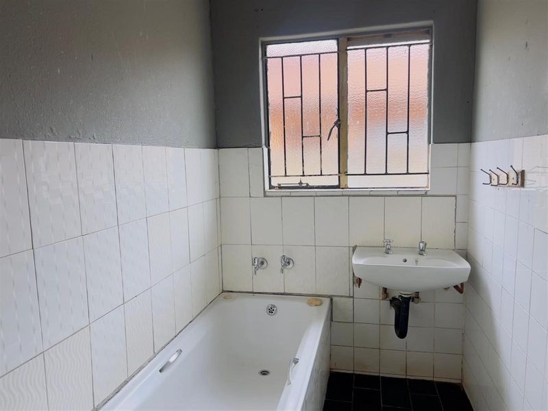 A functional bathroom featuring a bathtub, wall-mounted basin, and security bars on the window, requiring cosmetic updates to improve its overall condition.