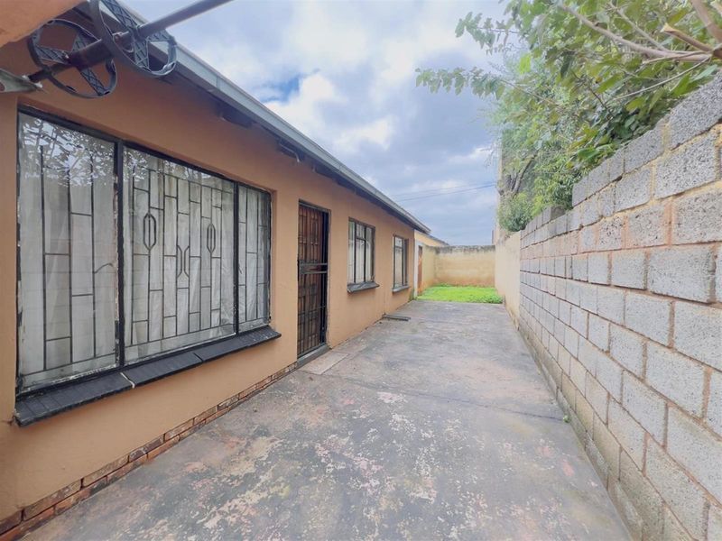 A rear exterior view of the property featuring a concrete paved walkway, perimeter boundary wall, and security-fitted windows and doors.