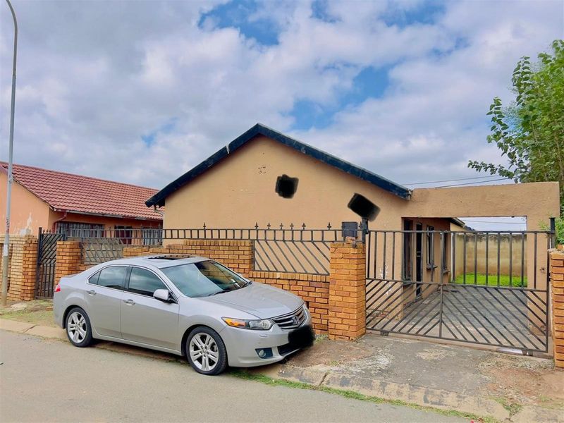 Front exterior view of a single-story house featuring a brick boundary wall, metal security gate, and a tiled roof.