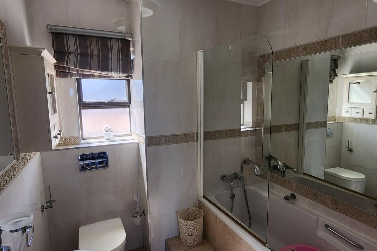 A functional bathroom featuring a combined bathtub and shower, wall-mounted toilet, and large vanity mirror with integrated lighting.