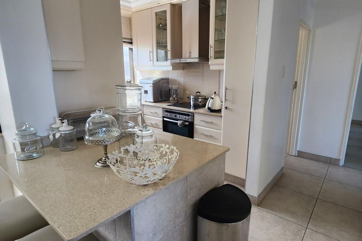 A functional kitchen featuring stone countertops, built-in cabinetry, an integrated oven and hob, and a breakfast bar area with tiled flooring.