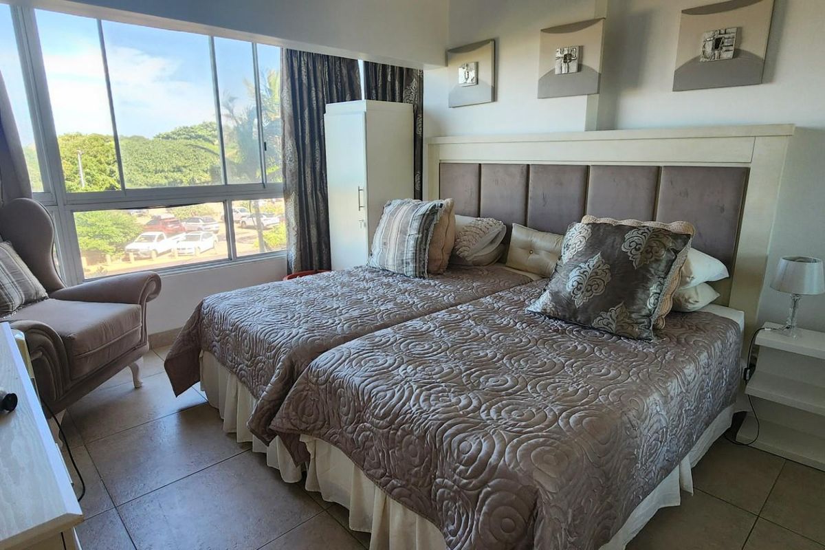 A well-lit bedroom featuring large windows with exterior views, tiled flooring, and a built-in headboard.