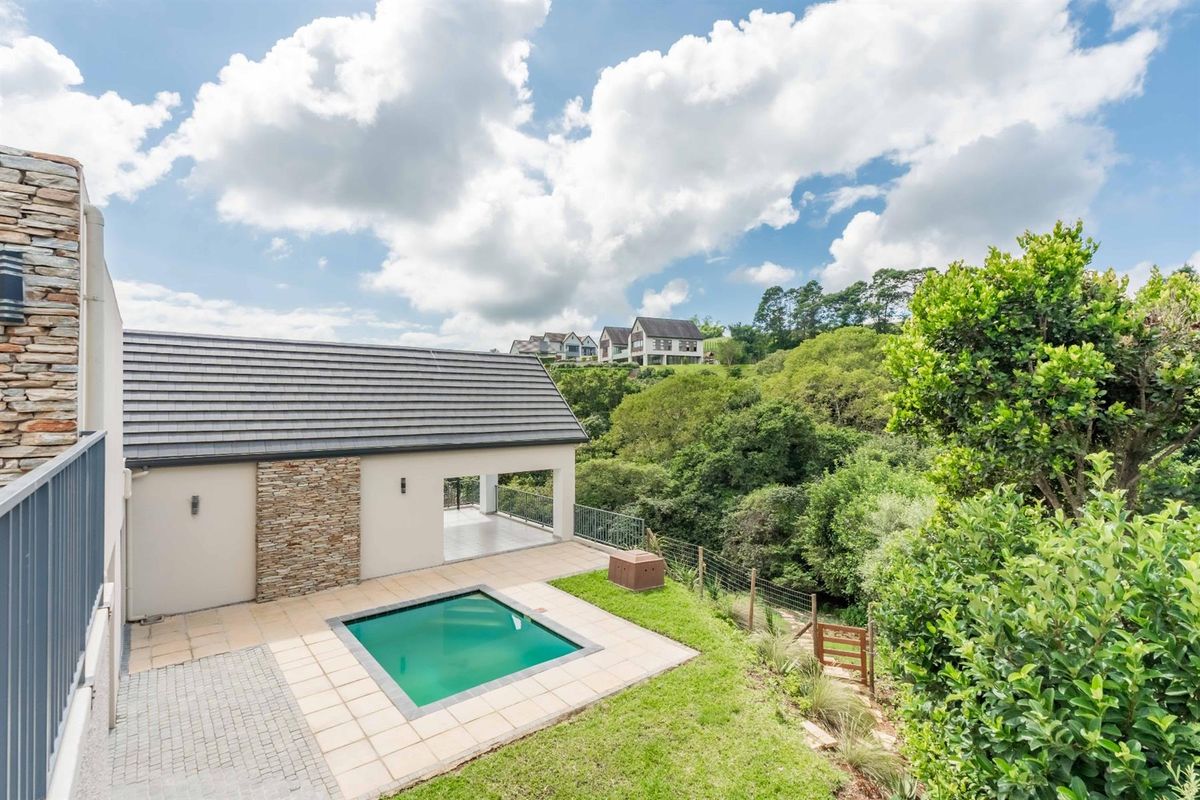 A well-maintained rear exterior featuring a tiled patio, a small swimming pool, and a landscaped garden overlooking a lush green valley.