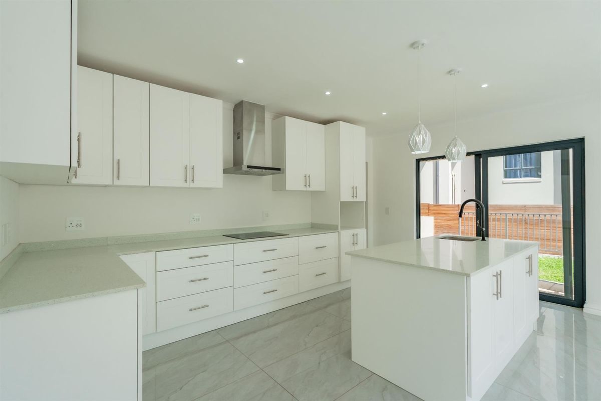 Modern kitchen featuring white cabinetry, stone countertops, a central island with a sink, and integrated stainless steel appliances, opening to an outdoor area.
