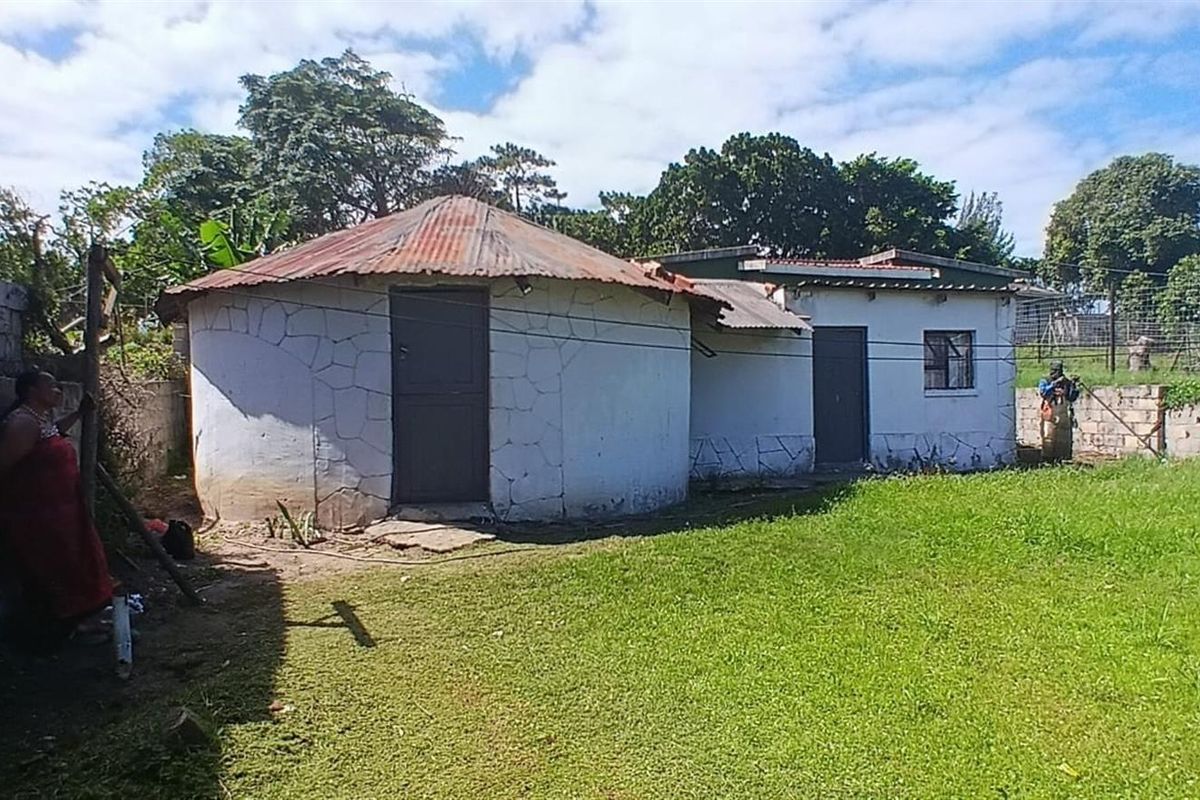 Rear view of a property featuring a traditional round structure with a corrugated metal roof and an adjacent rectangular building set within a garden.