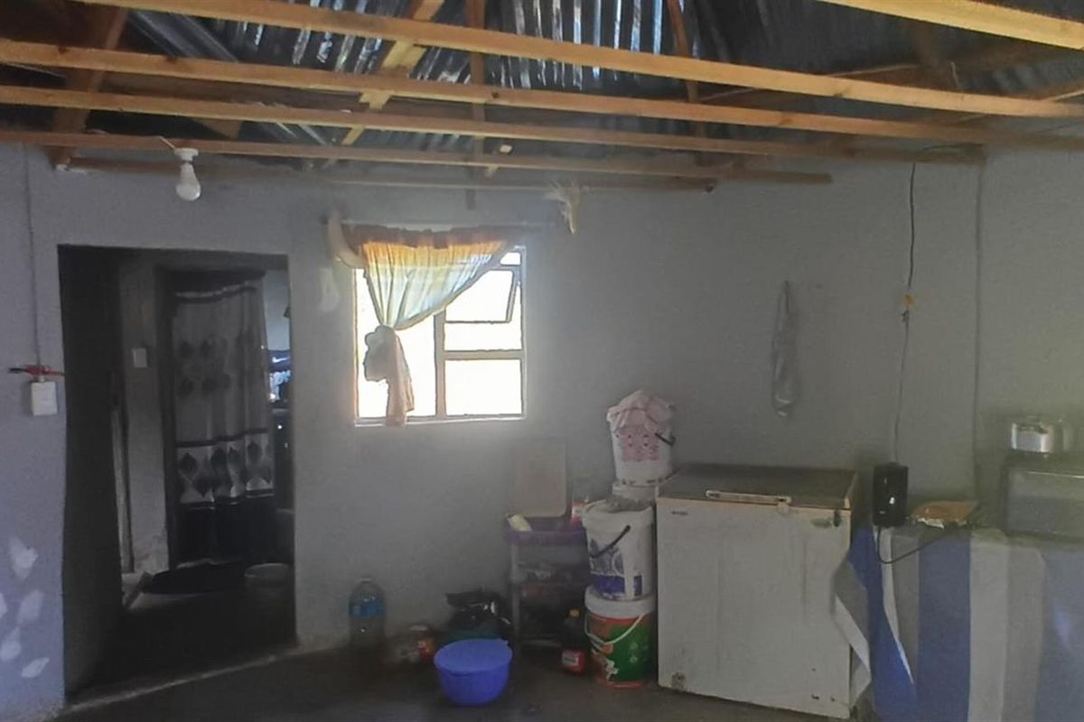 An interior living space featuring exposed timber roof trusses and corrugated metal roofing, requiring significant finishing and renovation to improve the overall condition.