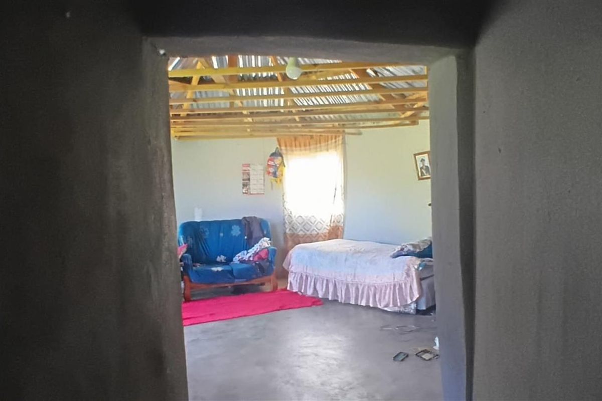 A bedroom space featuring an unfinished interior with exposed timber roof trusses, corrugated metal roofing, and a concrete floor.