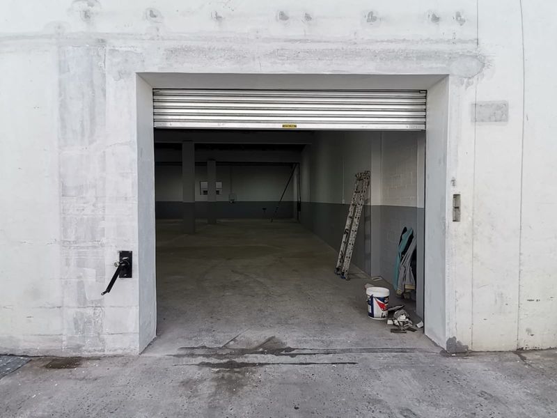 Industrial warehouse space featuring a large roller shutter door entrance, open-plan interior, concrete flooring, and structural support columns.