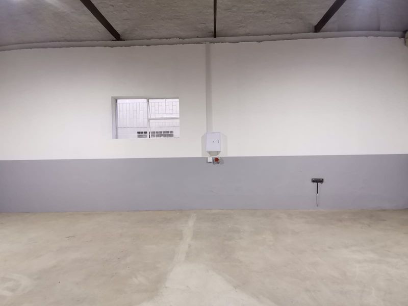 A spacious industrial utility area featuring concrete flooring, exposed ceiling beams, and a wall-mounted electrical distribution board.