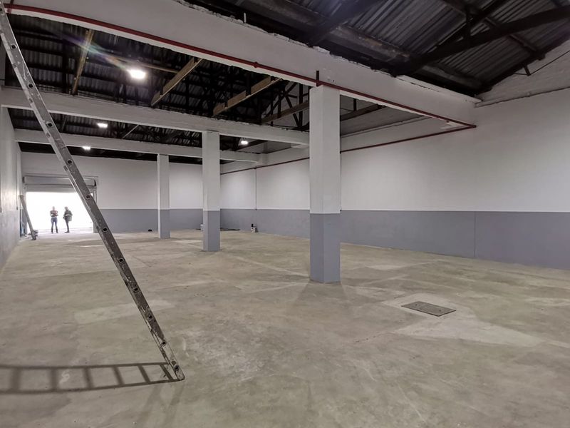 Spacious industrial warehouse unit featuring high ceilings, exposed structural beams, concrete flooring, and large roller shutter door access.