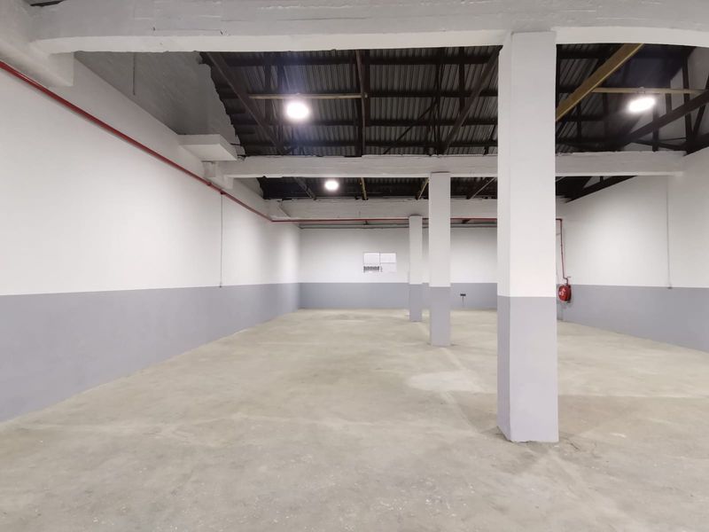 Spacious industrial warehouse unit featuring high ceilings, exposed structural beams, concrete flooring, and fire safety equipment.