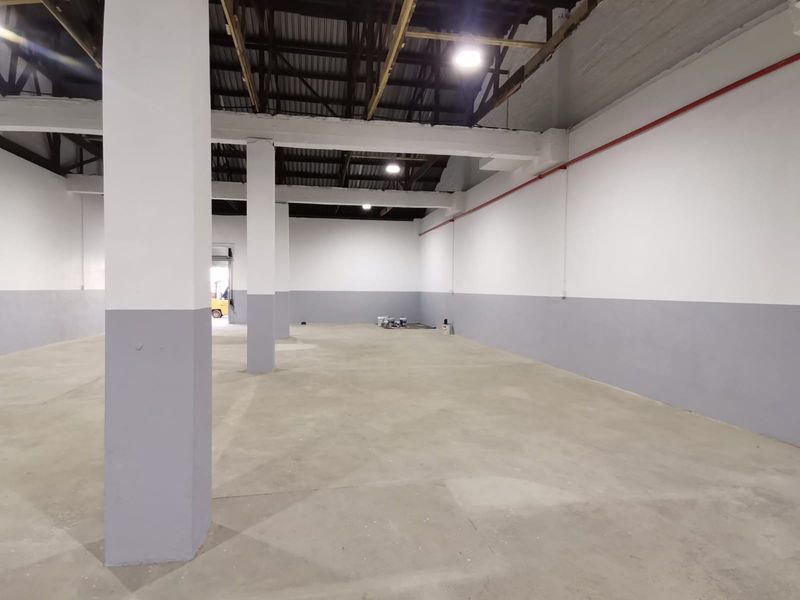 Spacious industrial warehouse interior featuring high ceilings, exposed structural beams, concrete flooring, and fire suppression piping.