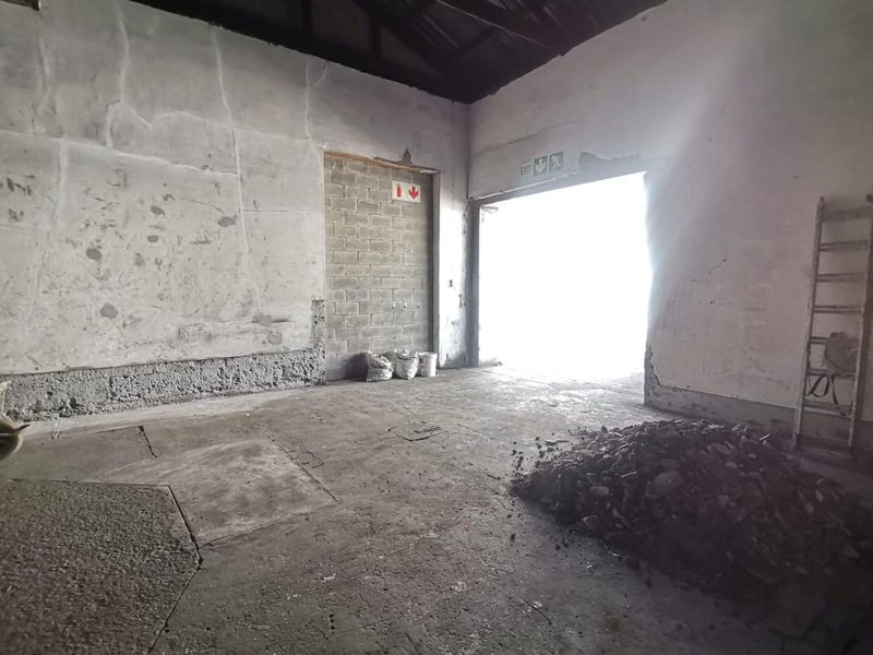 An industrial warehouse space featuring exposed brickwork, concrete flooring, and a large access doorway, currently in need of significant maintenance and repair.