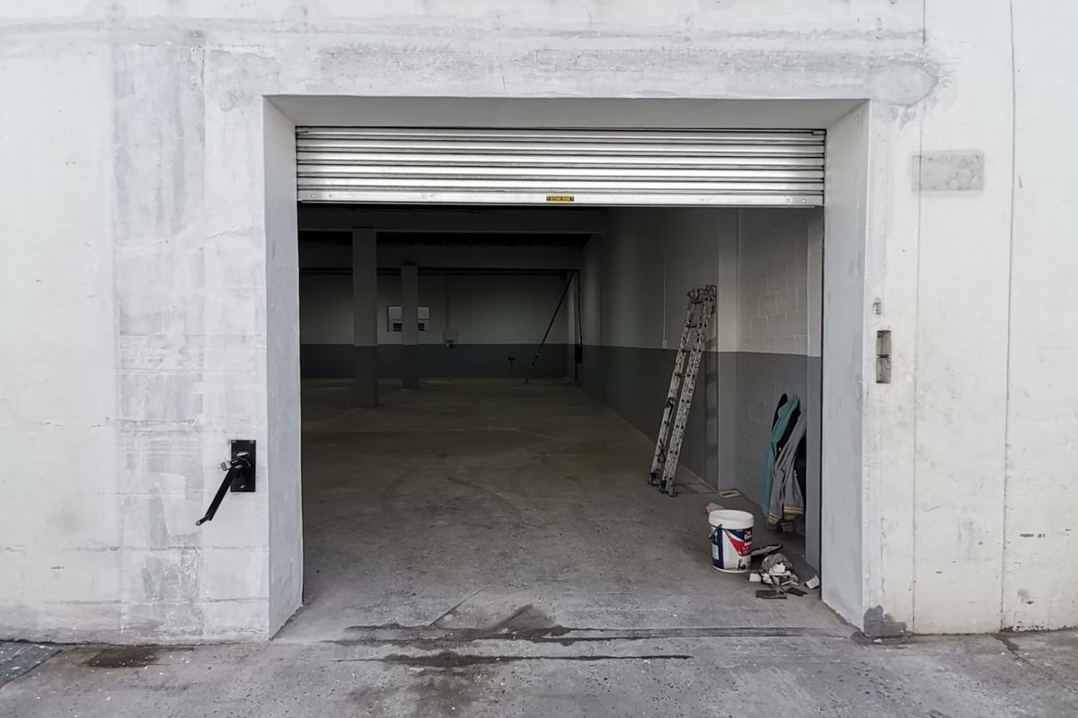 Industrial warehouse space featuring a large roller shutter door entrance, open-plan interior, concrete flooring, and structural support columns.