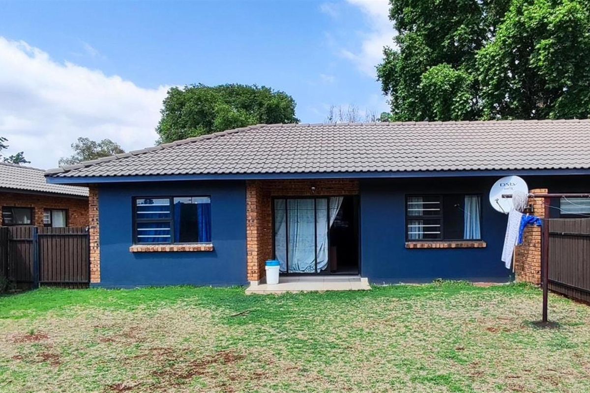 Rear view of the property featuring a blue painted facade, tiled roof, sliding glass door, and a private backyard area with perimeter fencing.