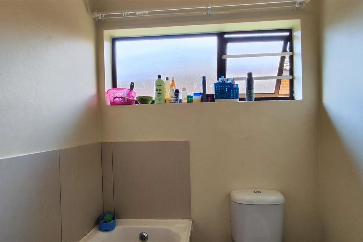 A functional bathroom featuring a toilet and a bathtub with tiled splashbacks and a horizontal window.