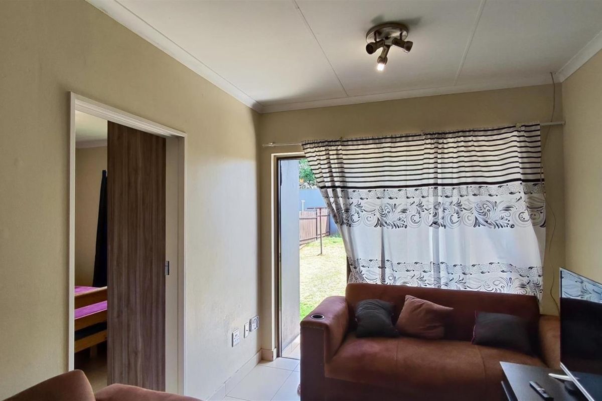 A living room featuring tiled flooring, a sliding door leading to the garden, and a wood-finish interior door.
