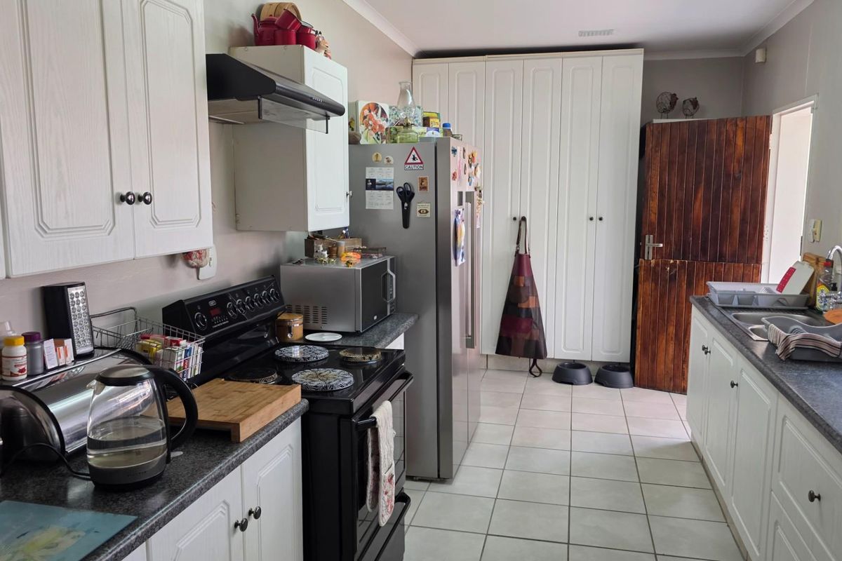A functional kitchen featuring white cabinetry, dark laminate countertops, tiled flooring, and a built-in pantry, offering ample storage and workspace.