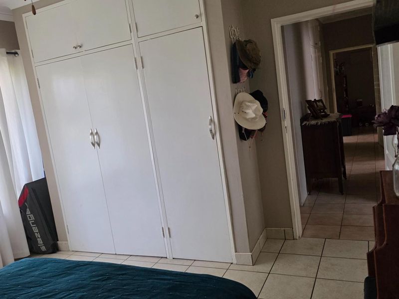 A bedroom featuring built-in cupboards and tiled flooring, with a view leading into the hallway.