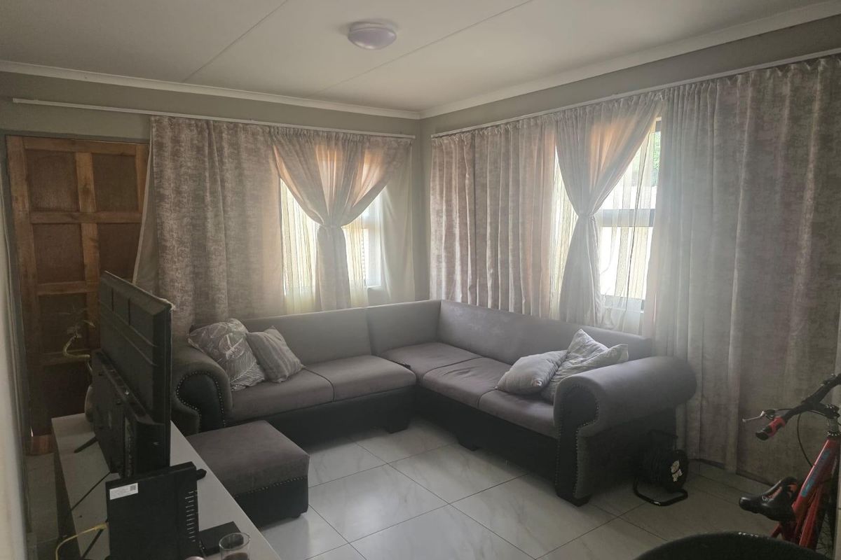 A living room featuring tiled flooring, neutral wall tones, and natural light through window treatments.