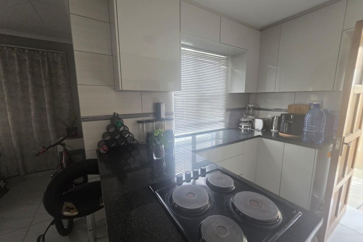 Modern kitchen featuring sleek white cabinetry, dark granite countertops, and a built-in electric hob with a tiled backsplash.