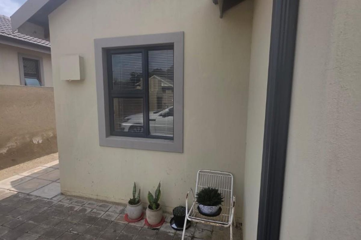 A side exterior view of the property featuring paved flooring, an aluminium window frame, and a downpipe along the wall.