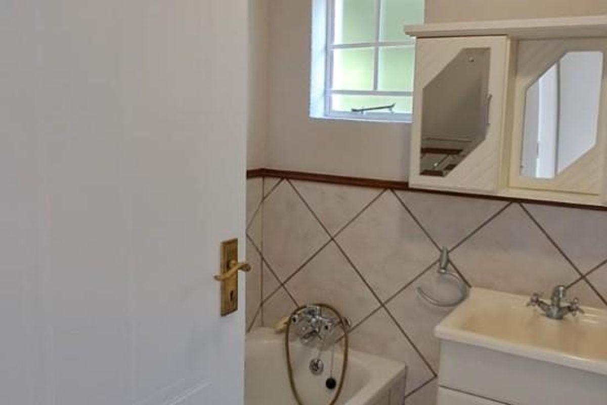 A functional bathroom featuring a built-in bathtub, vanity basin with storage, and tiled flooring in a retirement village setting.