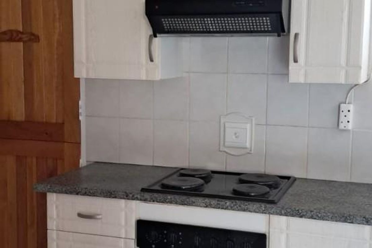A functional kitchen area featuring white cabinetry, a built-in oven, electric hob, extractor fan, and tiled flooring.