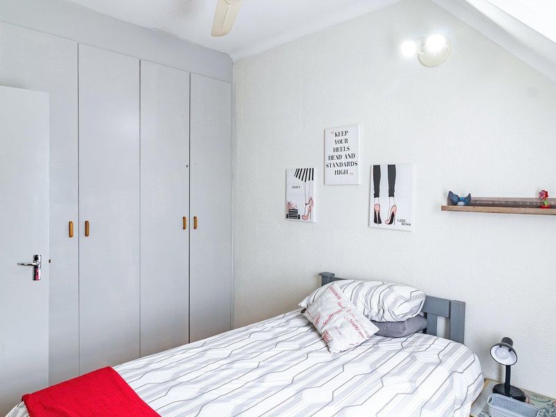 A bedroom featuring built-in cupboards, a sloped ceiling, and a ceiling fan, providing functional storage and overhead ventilation.