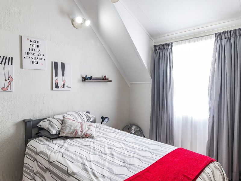 A cozy bedroom featuring a sloped ceiling and a window with fitted curtains, providing natural light to the space.