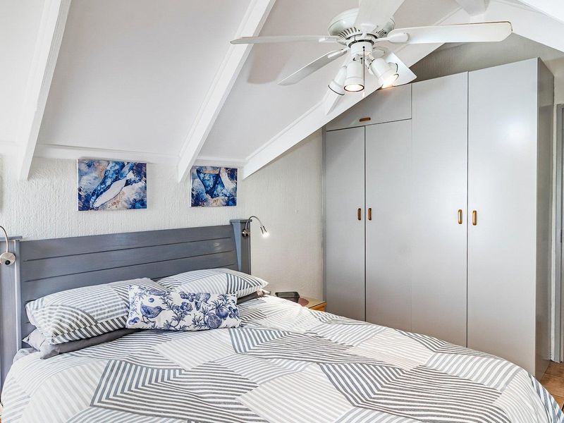 A cozy bedroom featuring a vaulted ceiling with exposed rafters, a ceiling fan, and built-in wardrobe storage.