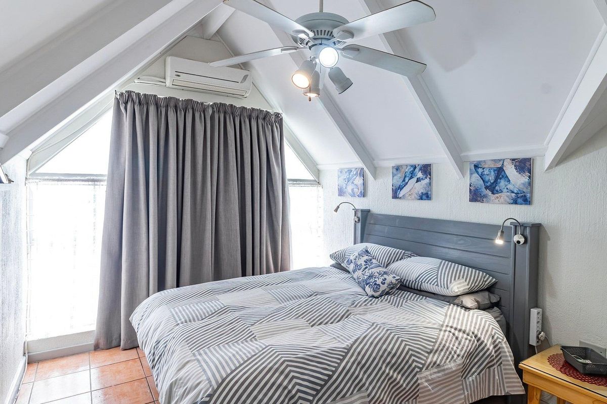 A cozy bedroom featuring a vaulted ceiling with exposed rafters, a ceiling fan, and a split-system air conditioner for climate control.