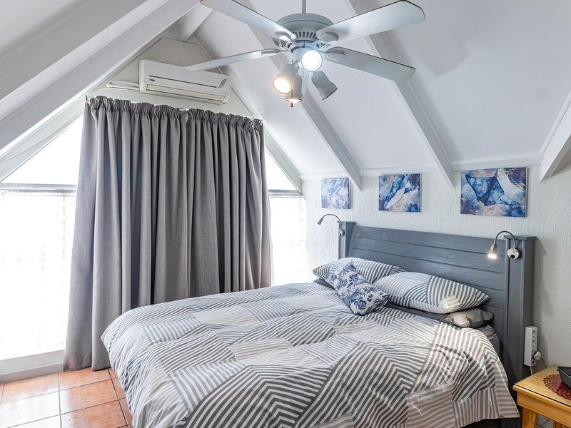 A cozy bedroom featuring a vaulted ceiling with exposed rafters, a ceiling fan, and a split-system air conditioner for climate control.