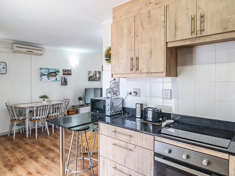 Open-plan kitchen and dining area featuring wood-look cabinetry, black granite countertops, built-in oven, electric hob, and wall-mounted air conditioning.